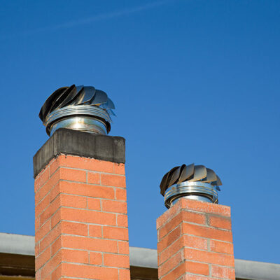 Two Brick Chimneys Topped with Metal Caps Against a Clear Blue Sky in Glen Burnie, MD