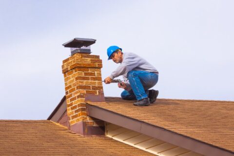 Contractor Builder with blue hardhat on the roof caulking chimney